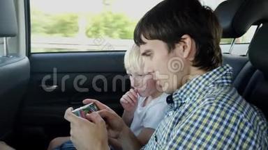 父亲和儿子坐在汽车座椅上，一边玩智能手机一边在后座上开车